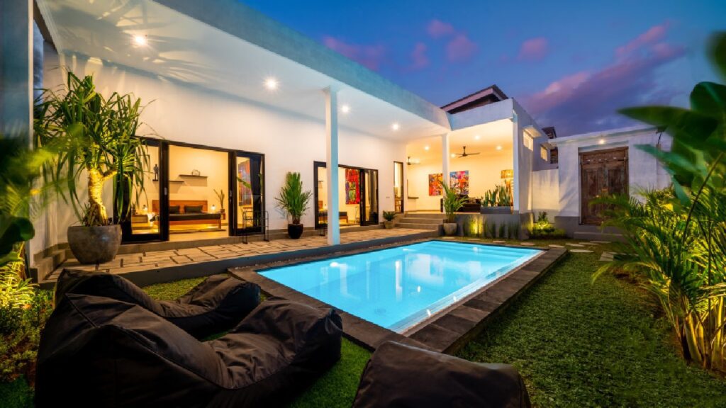 Modern home showcasing ways to blend indoor and outdoor pool design, featuring an open-plan layout, sliding glass doors, and a backyard swimming pool seamlessly connected to the interior living space at dusk